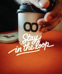 A hand closing a Loop takeaway cup on an orange counter, 'Stay in the loop' written across it