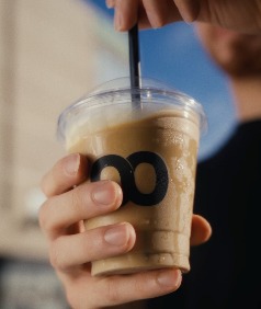 An iced latte in a Loop cup, a straw being stirred